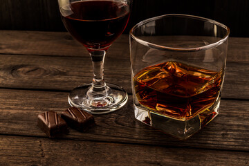 Glass of brandy and red wine with two chocolate candies on an old wooden table. Angle view