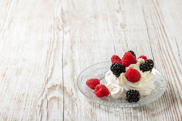 Pavlova's cake on a glass plate on a light wooden table. Cake with meringues, raspberries and blackberries. High quality photo