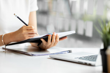 Fototapeta premium An Asian female is taking notes on her notebook for online classes, study ideas and note-taking.