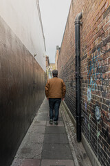 Hombre joven de espaldas caminando hacia el final de una calle estrecha
