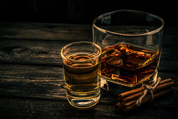 Glass of brandy and tequila with cinnamon sticks tied with jute rope on an old wooden table. Angle view