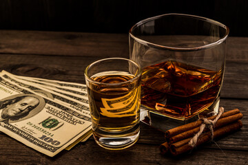 Glass of brandy and tequila with money and cinnamon sticks tied with jute rope on an old wooden table. Angle view