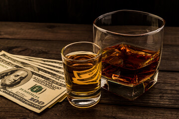 Glass of brandy and tequila with money on an old wooden table. Angle view