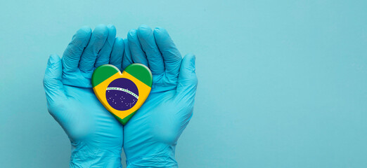 Doctors hands wearing surgical gloves holding Brazil flag heart