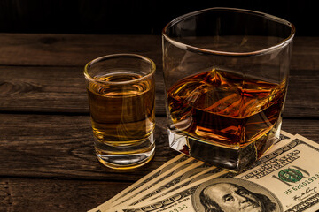 Glass of brandy and tequila with money on an old wooden table. Angle view