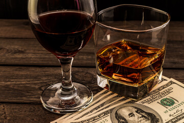 Glass of brandy and red wine with money on an old wooden table. Angle view