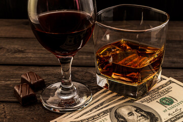 Glass of brandy and red wine with money and chocolate on an old wooden table. Angle view