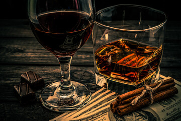 Glass of brandy and red wine with money and  chocolate with cinnamon sticks tied with jute rope on an old wooden table. Angle view