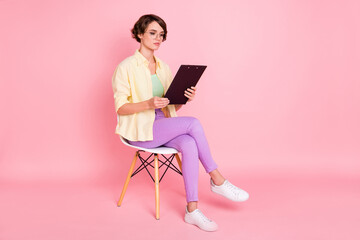 Photo of serious sweet young woman wear yellow shirt arm glasses sitting chair reading documents isolated pink color background