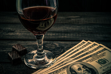 Glass of red wine and chocolate with money on an old wooden table. Angle view