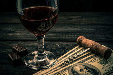 Glass of red wine and chocolate with money and corkscrew  on an old wooden table. Angle view
