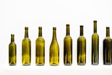 Glass bottles of different shapes and sizes stand in a row on a gray background. Production of packaging for bottling alcoholic beverages