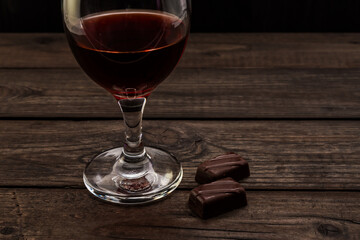 Glass of red wine with chocolate on an old wooden table. Close up view