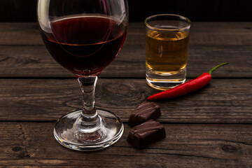 Glass of red wine and tequila with chocolate and cayenne pepper on an old wooden table. Close up view