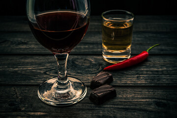 Glass of red wine and tequila with chocolate and cayenne pepper on an old wooden table. Close up view