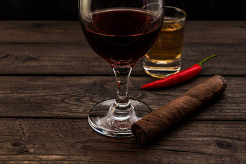 Glass of red wine and tequila with cuban cigar and cayenne pepper on an old wooden table. Close up view, focus on the cuban cigar