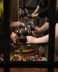 Women clinking with glasses of red wine. Friendly toast at festive dinner in restaurant. Group of women celebrating an event togetherShot through window. Alcoholic drink.