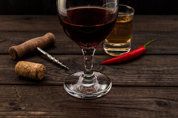 Glass of red wine and tequila with corkscrew and cayenne pepper on an old wooden table. Close up view, focus on the glass of red wine