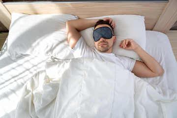 A man sleeps in a bed with a mask in front of his eyes