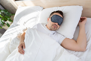 A man sleeps in a bed with a mask in front of his eyes