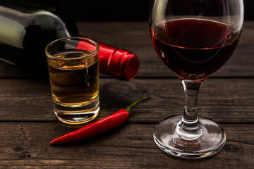 Glass and bottle of red wine and tequila with cayenne pepper on an old wooden table. Close up view, focus on the glass of red wine