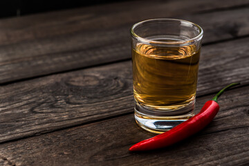 Glass of tequila with cayenne pepper on an old wooden table. Close up view
