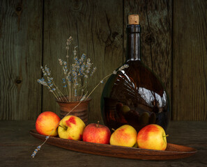 Still life with ripe apples, a large brown glass bottle and a bouquet of lavender in a ceramic vase. Vintage.