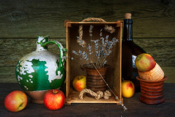 Still life with an old ceramic jug with peeling paint, a large dark brown glass bottle, a ceramic vase, a bunch of lavender and ripe apples. Vintage.