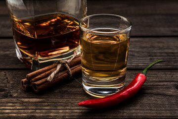 Glass of brandy and tequila with cayenne pepper and cinnamon sticks tied with jute rope on an old wooden table. Close up view