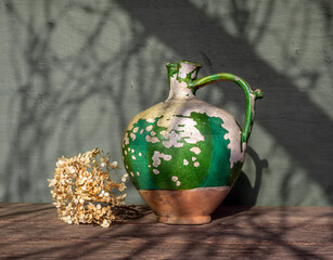 Very old ceramic jug with peeling paint and dried flowers. Vintage.