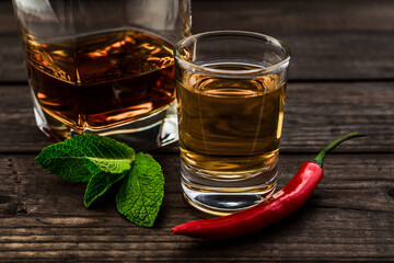 Glass of brandy and tequila with cayenne pepper and mint sprig on an old wooden table. Close up view
