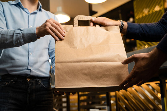 Man in shirt picking a takeaway food bag from a restaurant. Blank craft paper box with room for text or logo. Crop shot, unrecognizable faces.