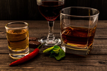 Three glasses with brandy, tequila and red wine with mint sprig, chocolate and cayenne pepper on an...