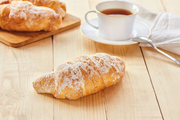 Tasty croissants with powdered sugar for the breakfast on wooden board. Traditional french pastry on the breakfast. Close up view