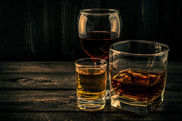 Three glasses with brandy, tequila and red wine on an old wooden table. Angle view