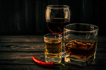 Three glasses with brandy, tequila and red wine with cayenne pepper on an old wooden table. Angle...