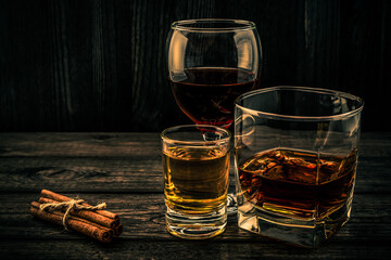 Three glasses with brandy, tequila and red wine with cinnamon sticks tied with jute rope on an old wooden table. Angle view