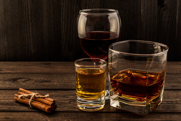 Three glasses with brandy, tequila and red wine with cinnamon sticks tied with jute rope on an old wooden table. Angle view