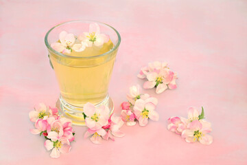 Natural remedy for skincare with apple blossom flowers with hot drink in a glass on pink marble. Can clear acne, provide a clear complexion & help with other skin problems. High in antioxidants.