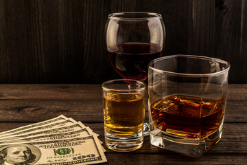 Three glasses with brandy, tequila and red wine with money on an old wooden table. Angle view