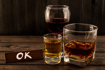 Three glasses with brandy, tequila and red wine with the wooden plank on it is an inscription 
