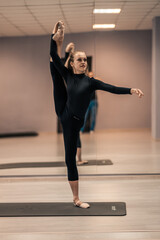 Obraz premium Beautiful young woman is engaged in gymnastics in the gym. The athletic body of the girl is covered with tight-fitting yoga clothes.