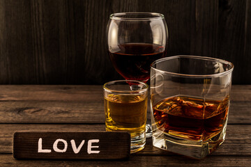 Three glasses with brandy, tequila and red wine with the wooden plank on it is an inscription 