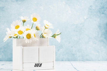 cube calendar for July with daisy flowers over blue background
