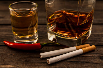 Glass of brandy and tequila with cayenne pepper and cigarettes on an old wooden table. Close up view, focus on the cigarettes