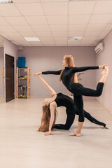 Beautiful young woman is engaged in gymnastics in the gym. The athletic body of the girl is covered with tight-fitting yoga clothes.