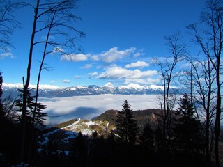 Panoramic view of Kamnik-Savinja alps and Stortic mountain in Gorenjska, Slovenia in winter and fog covering the basin bellow and church at Jamnik