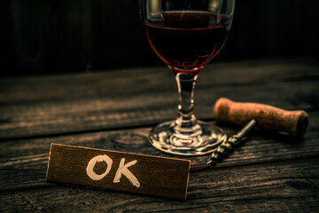 Glass of red wine with corkscrew and the wooden plank on it is an inscription 