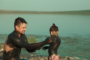 therapeutic mud for the body. mud baths on the lake. a man and a child are smeared with clay....