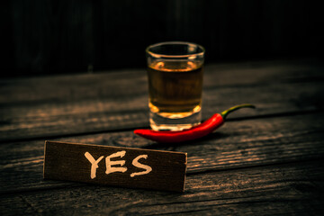 Glass of tequila with cayenne pepper and the wooden plank on it is an inscription 